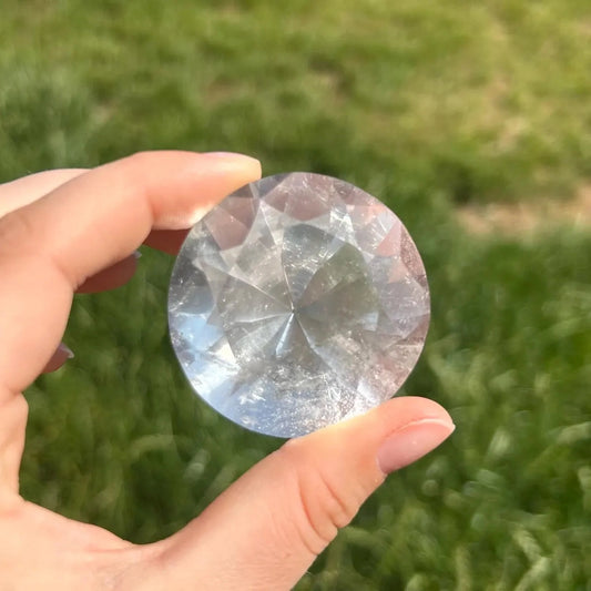 front view of 300ct flawless brazilian clear quartz round brilliant faceted gemstone held in hand outdoors - clearquartzshop
