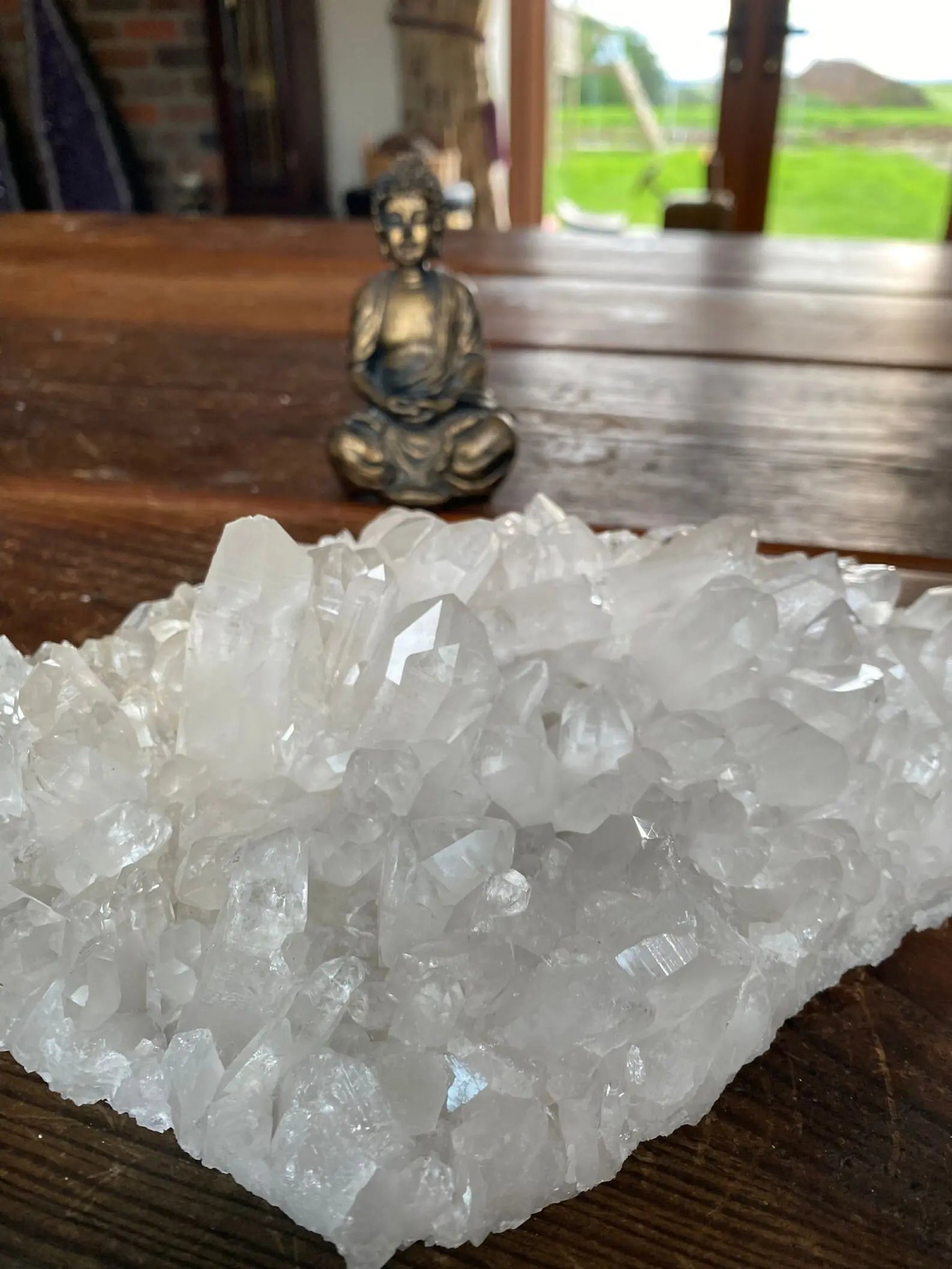 natural clear quartz cluster with buddha statue in background, raw formation from brazil - clearquartzshop