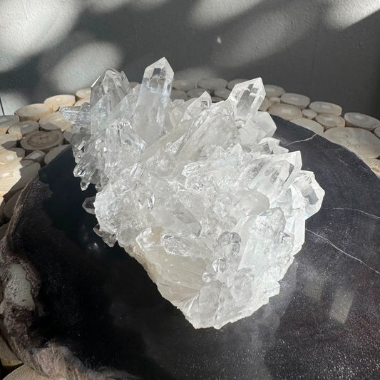 large clear quartz crystal cluster on black surface, displayed under natural light - healing crystal from clearquartzshop